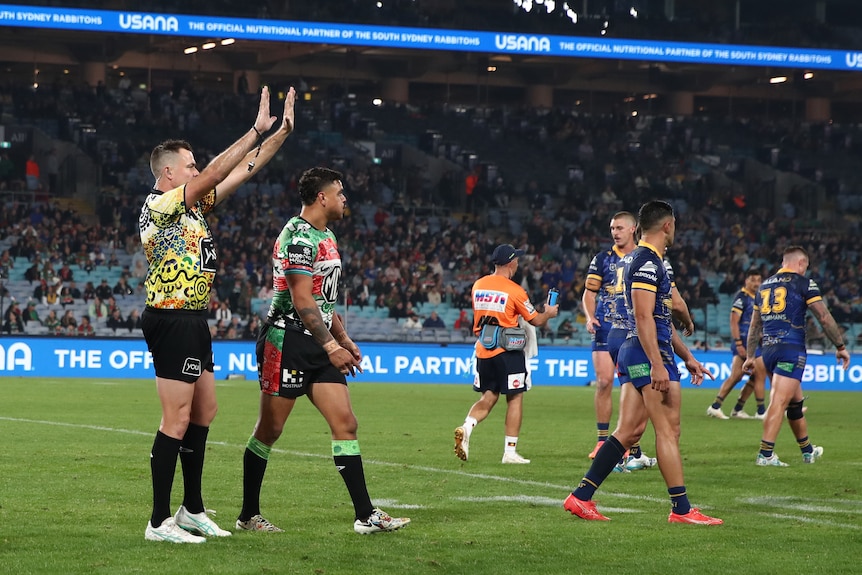An NRL referee puts his hands in the air, sending a player to the sin-bin, who is walking off