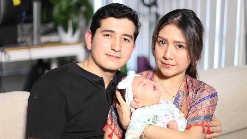 A man and woman sit on a couch holding a baby