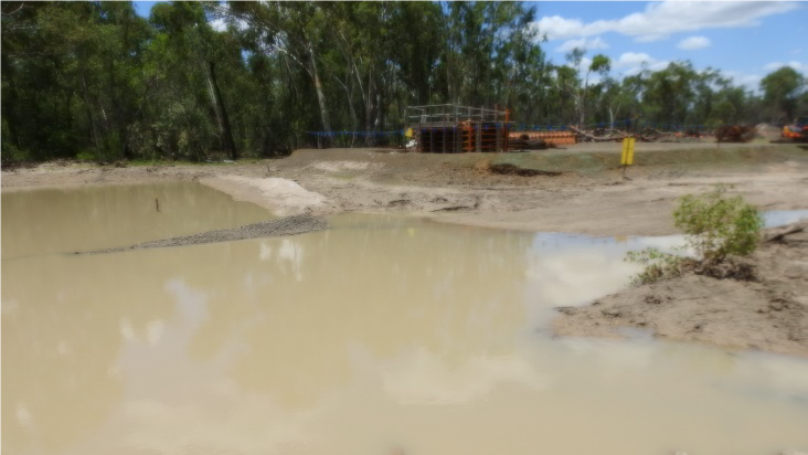 A creek with water and rocks over it, surrounded by construction equipment and a few trees.