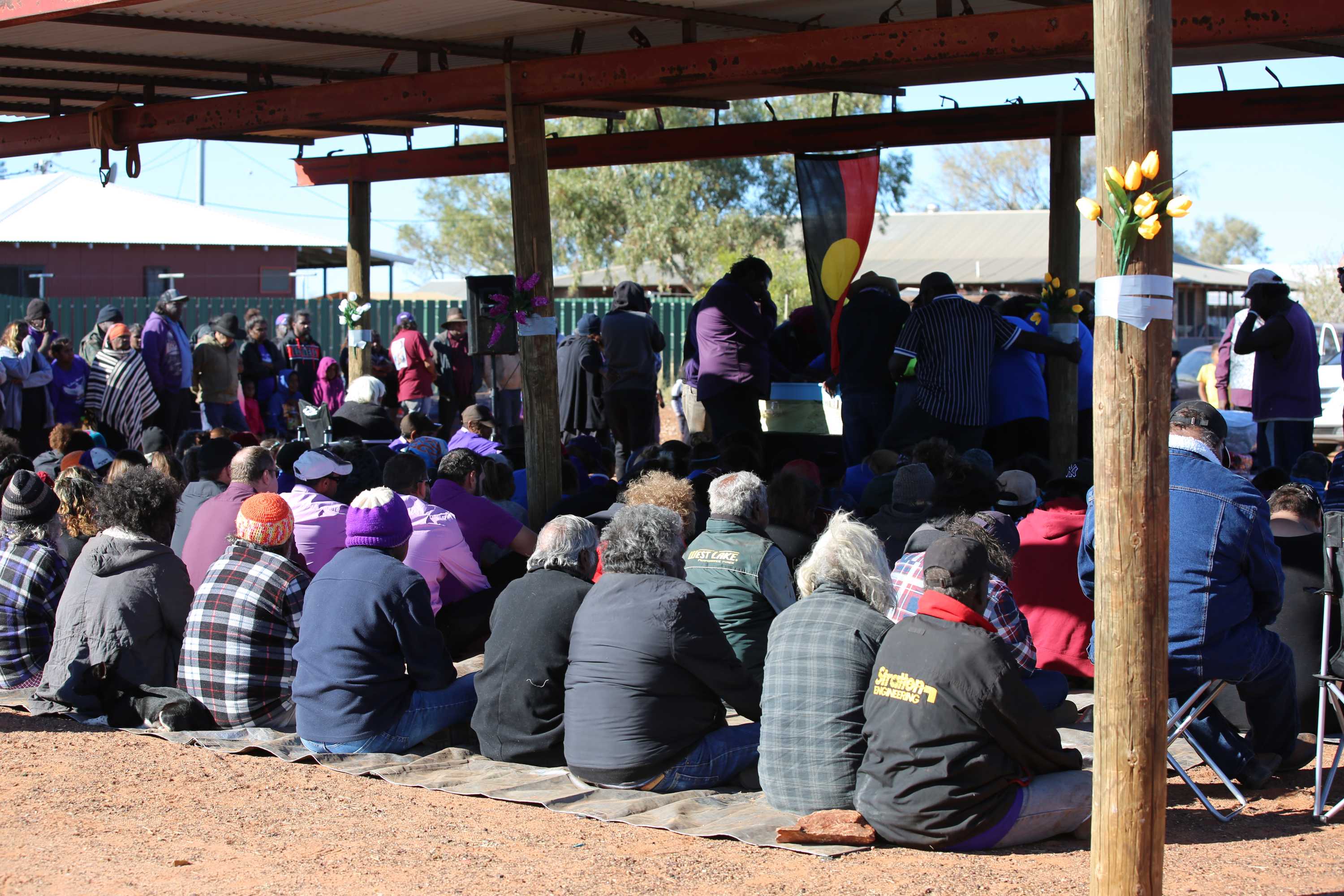 Mourners sit under a corrugated roof at Daisy Kadibil's funeral.
