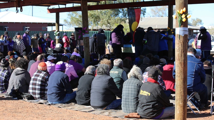 Mourners sit under a corrugated roof at Daisy Kadibil's funeral.