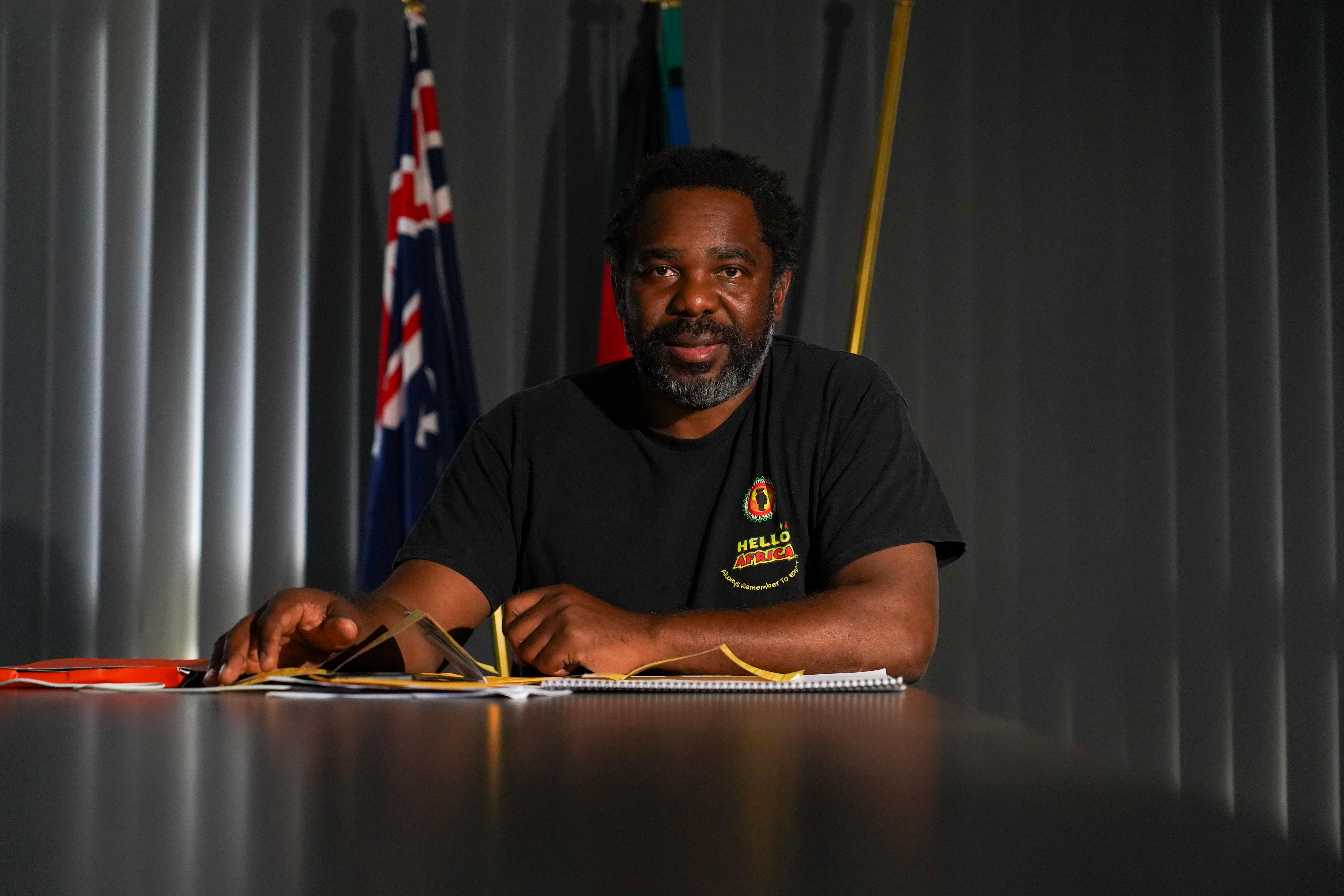 Black man sitting at desk with flags behind him