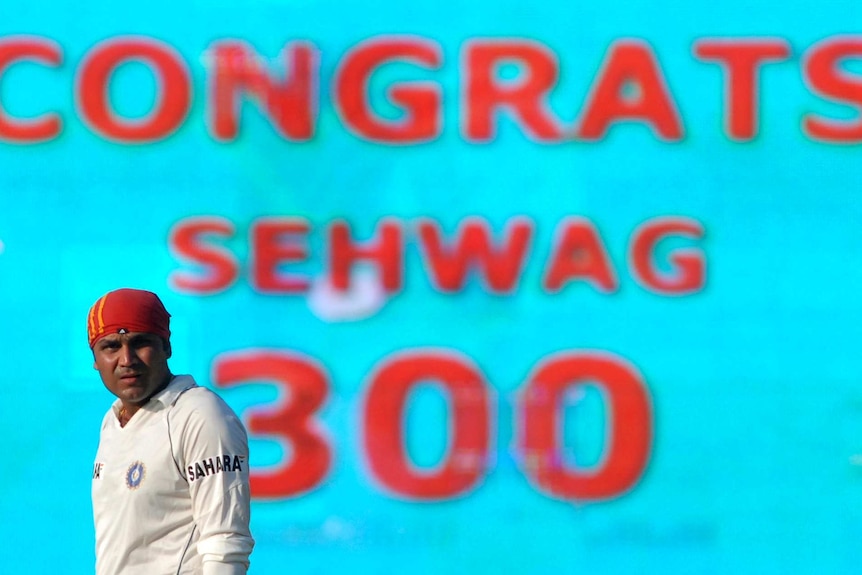 Virender Sehwag looks on as a screen behind him reads "Congrats Sehwag 300"