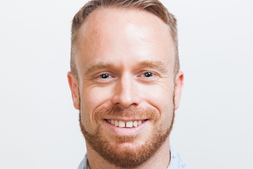 A close-up portrait of a man with red hair smiling at the camera.