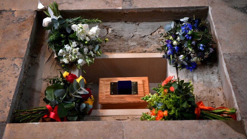 Bunches of flowers placed around ashes laid in a hole in the ground.