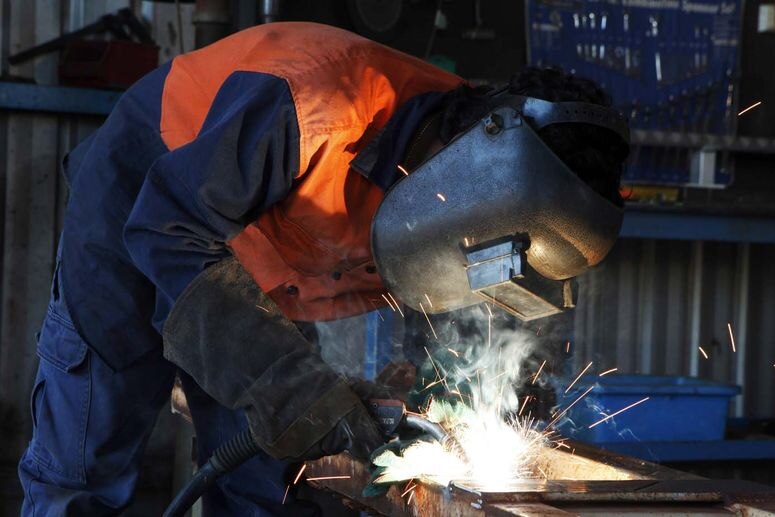 Sparks fly up towards the facemask of an aluminium welder as he works.