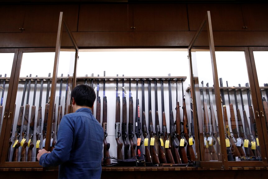Man looks at row of rifles on display in a cabinet.