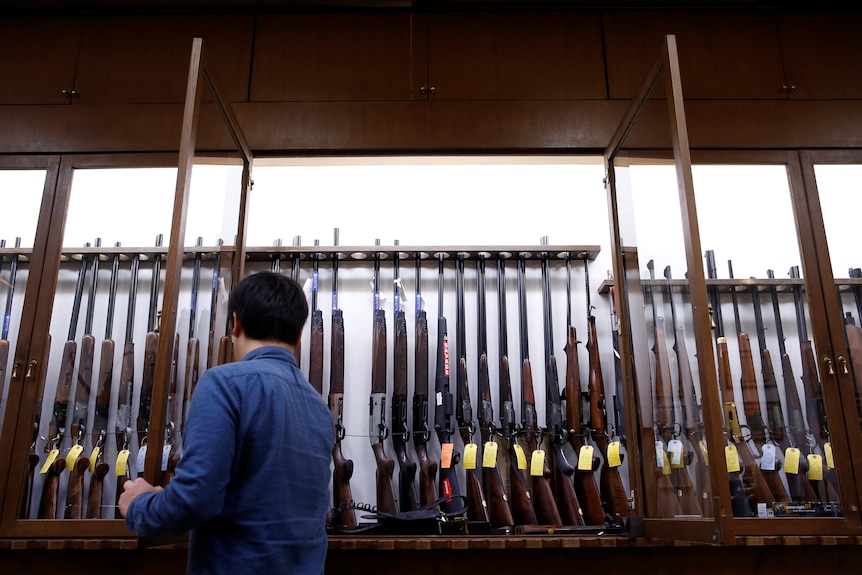 Man looks at row of rifles on display in a cabinet.