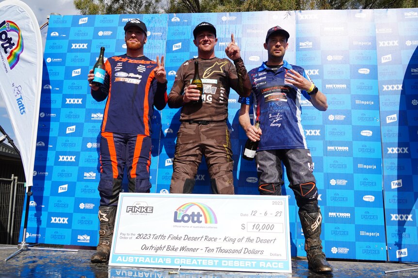 Three men in motorsport clothes standing on a podium.