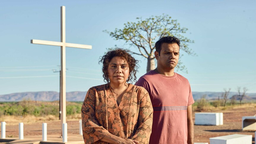 An Aboriginal woman and man stand in front of a cross in the desert in the tv show Mystery Road