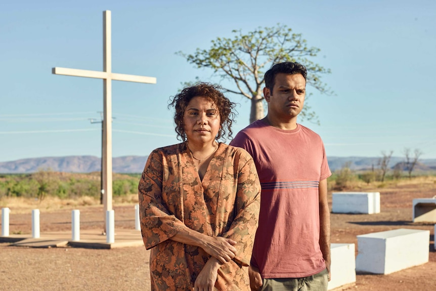 An Aboriginal woman and man stand in front of a cross in the desert in the tv show Mystery Road