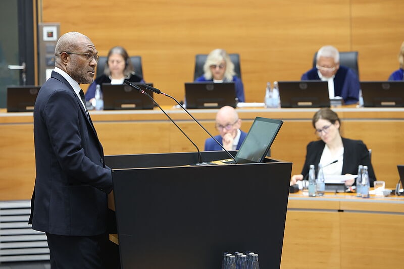 A man in suit and glasses speaking into mircophones in front of court.