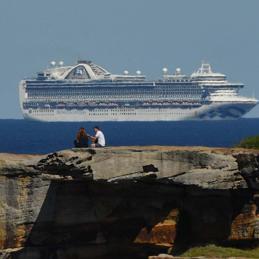 A couple sit on a rock with the ship on the horizon