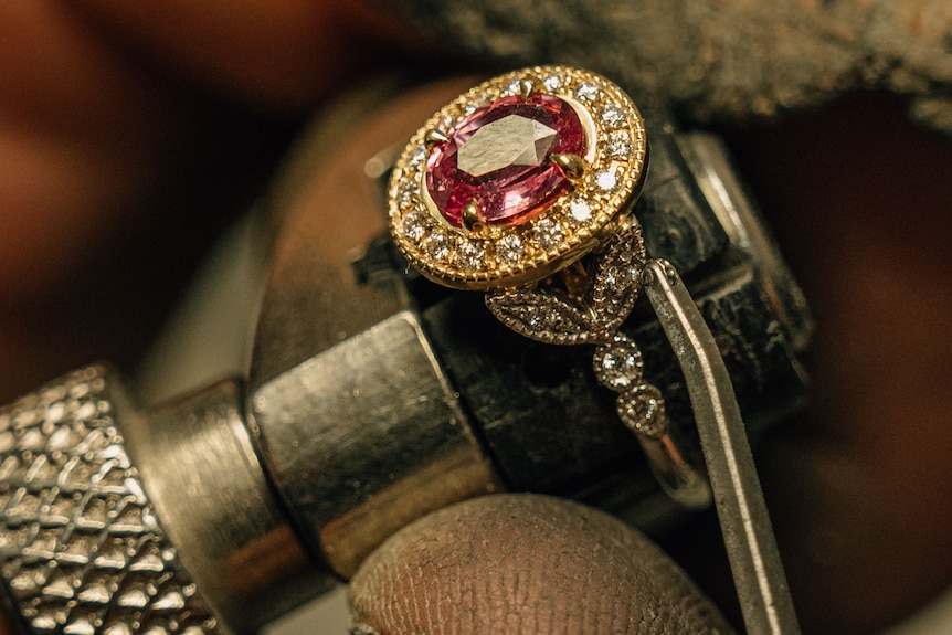 A close-up of jewellery with a large pink gemstone around a tool.