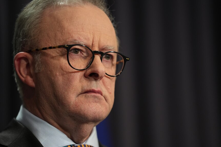 A closeup shot of the prime minister looking sombre, wearing glasses and frowning