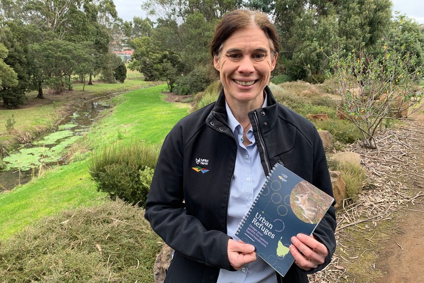 Kate Thorn stands holding a booklet in a landscaped garden.