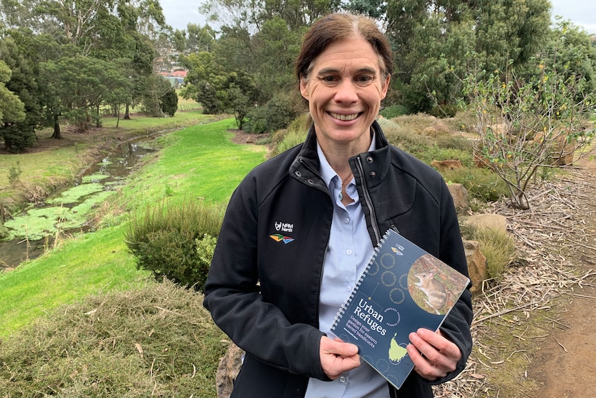 Kate Thorn stands holding a booklet in a landscaped garden.