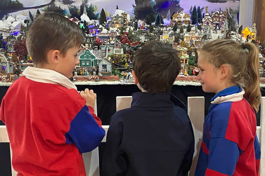 Three primary school aged children admire tiny Christmas village display.