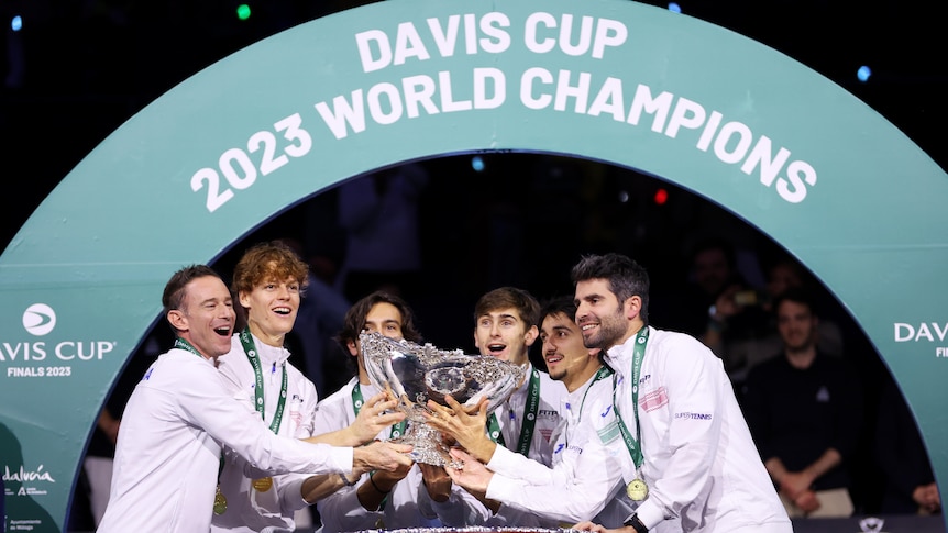 A group of Italian tennis players smile as they hold a trophy, with a sign saying "Davis Cup 2023 World Champions".