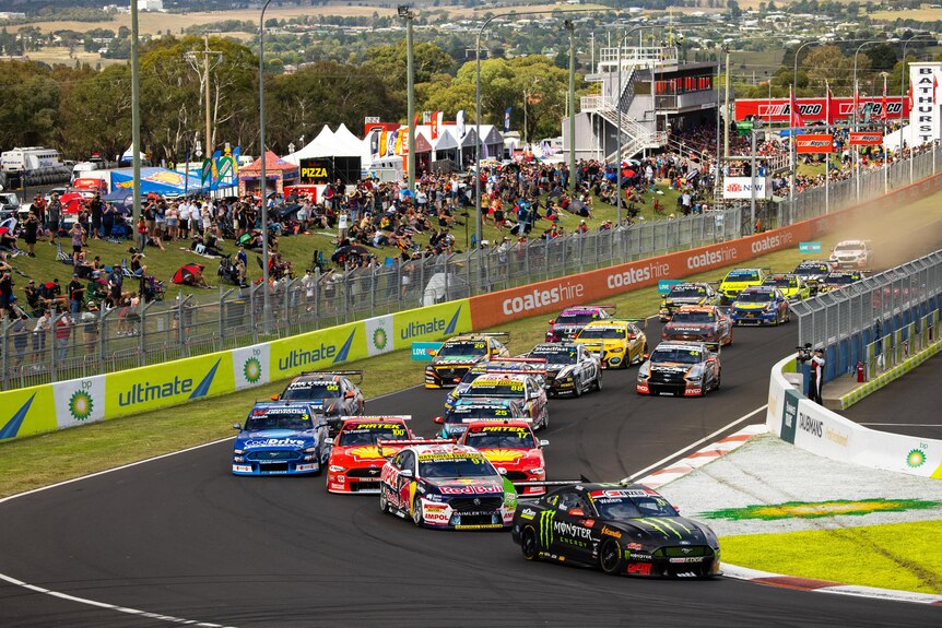 Cars turn around the first corner at the Mount Panorama circuit as fans watch on