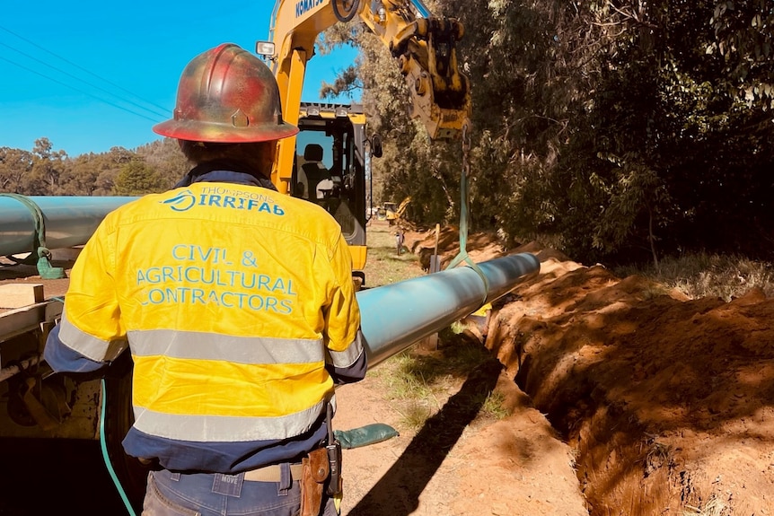 A man in a yellow high fix shirt and red hard hat works on the construction of a pipeline