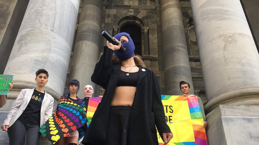 A masked member of Russian punk rock group Pussy Riot holds a microphone.