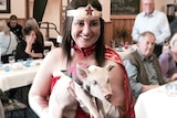Jacqui Lambie, dressed in a Wonder Woman costume, holds a piglet.