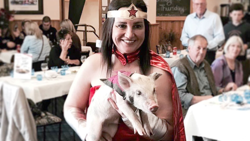 Jacqui Lambie, dressed in a Wonder Woman costume, holds a piglet.