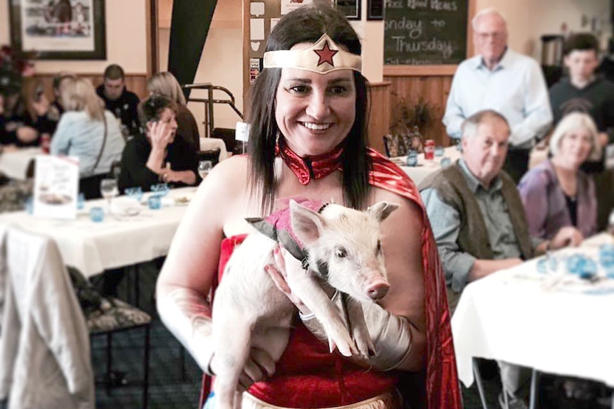 Jacqui Lambie, dressed in a Wonder Woman costume, holds a piglet.