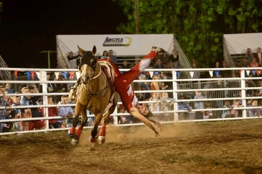 Girl hanging upside down off horse in rodeo ring