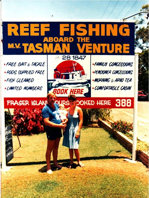 A photo taken in the 1980s of a man and a woman with their baby daughter standing in front of a fishing charter sign