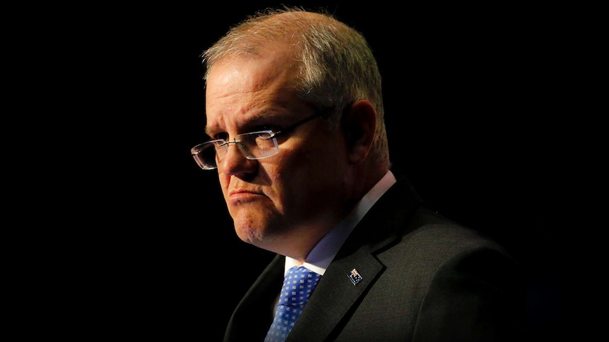 Scott Morrison frowns during a speech at Parliament House. The background is dark
