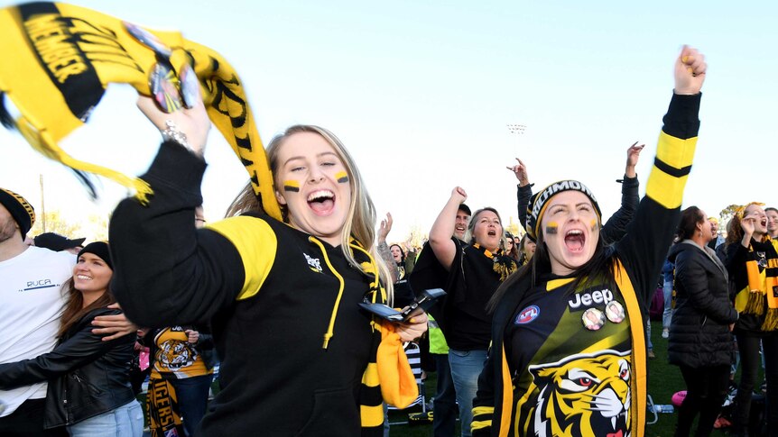 Two girls wear scarves and tigers accessories and jump and cheer at the end of the game.