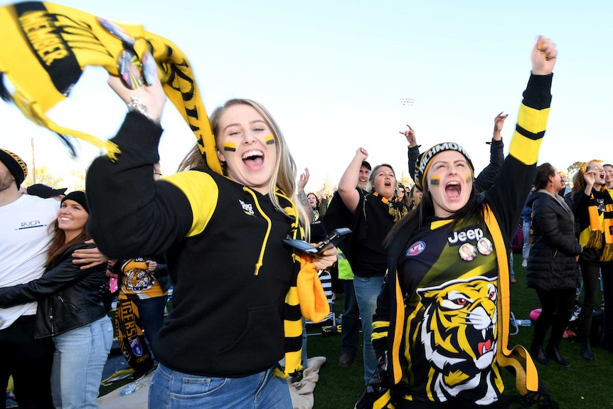 Two girls wear scarves and tigers accessories and jump and cheer at the end of the game.