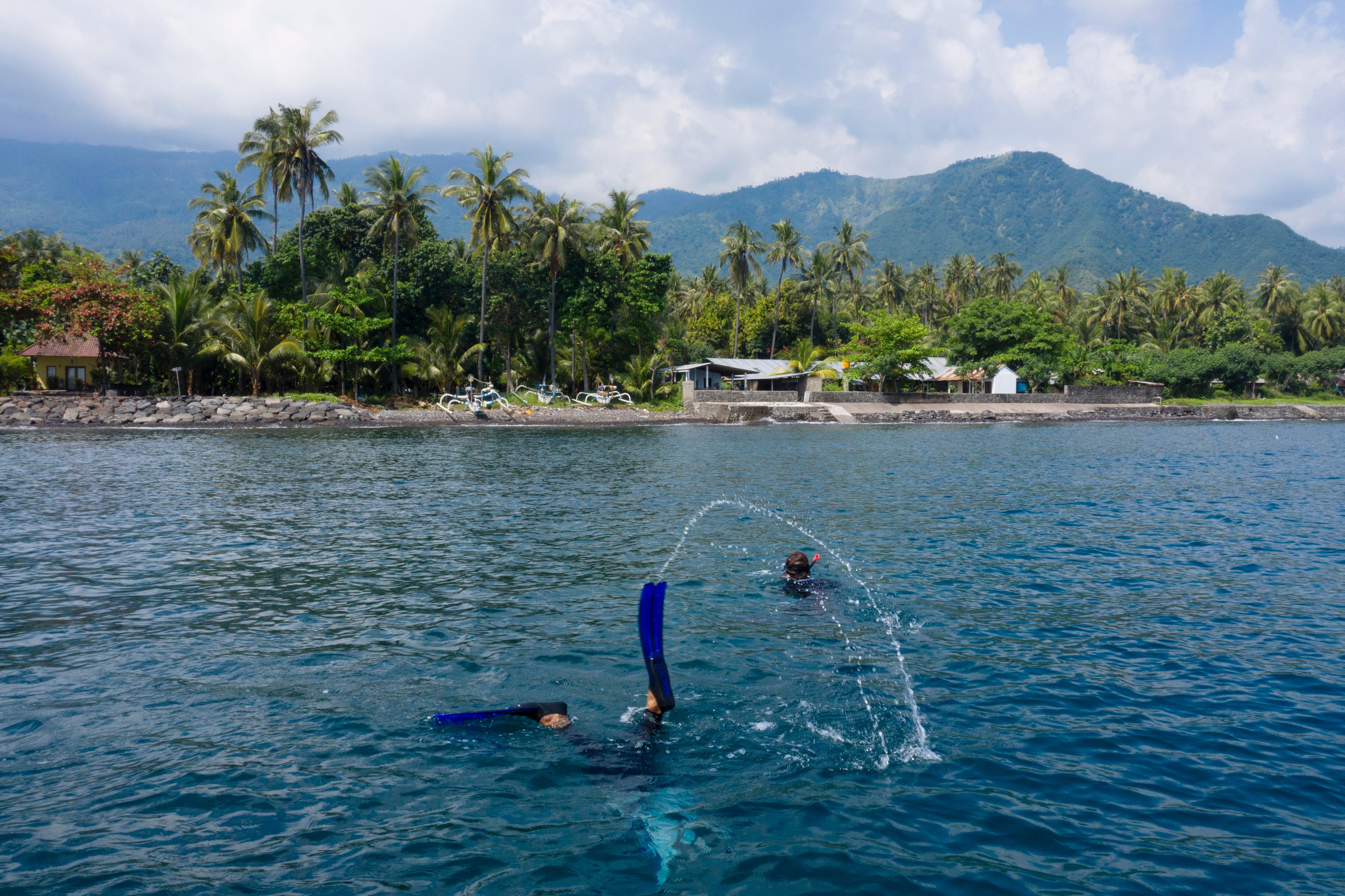 A scuba diver's flippers stick out of the water in front of a tropical island. 