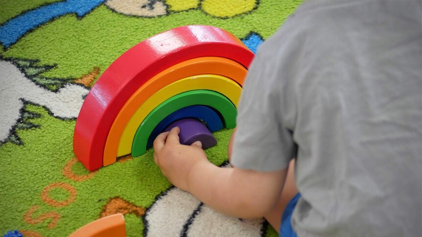 A child plays with a wooden block toy shaped like a rainbow