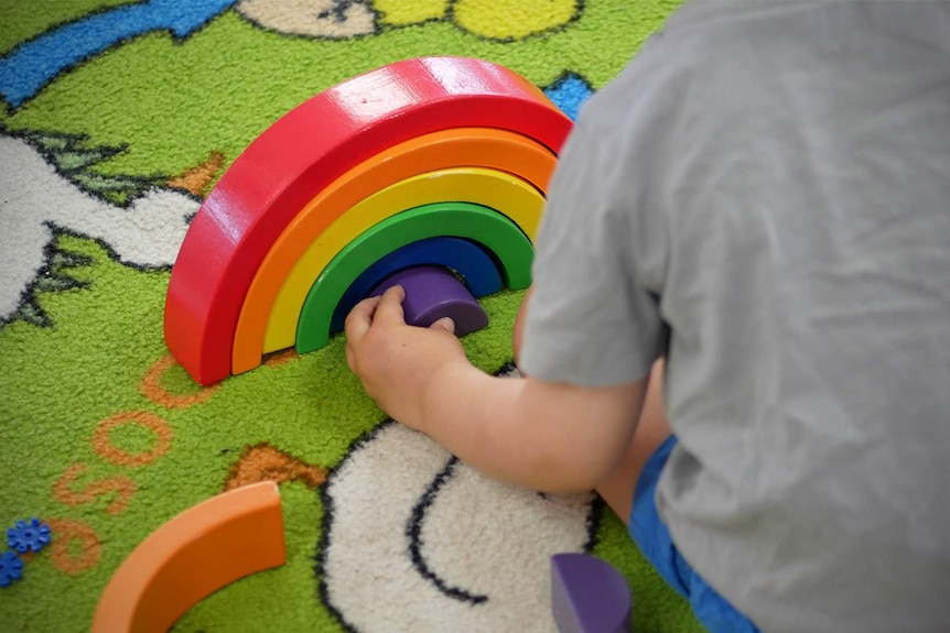 A child plays with a wooden block toy shaped like a rainbow