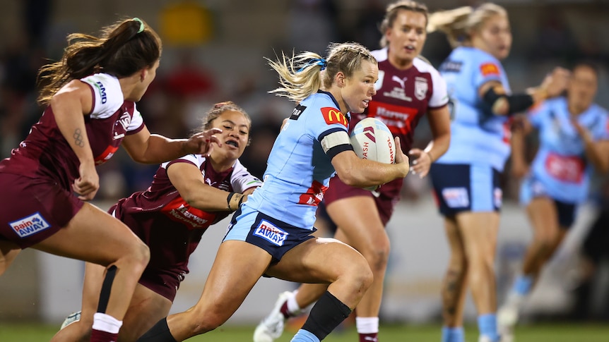 A NSW Women's rugby league player races up the field as Queensland players try to tackle her in State of Origin.