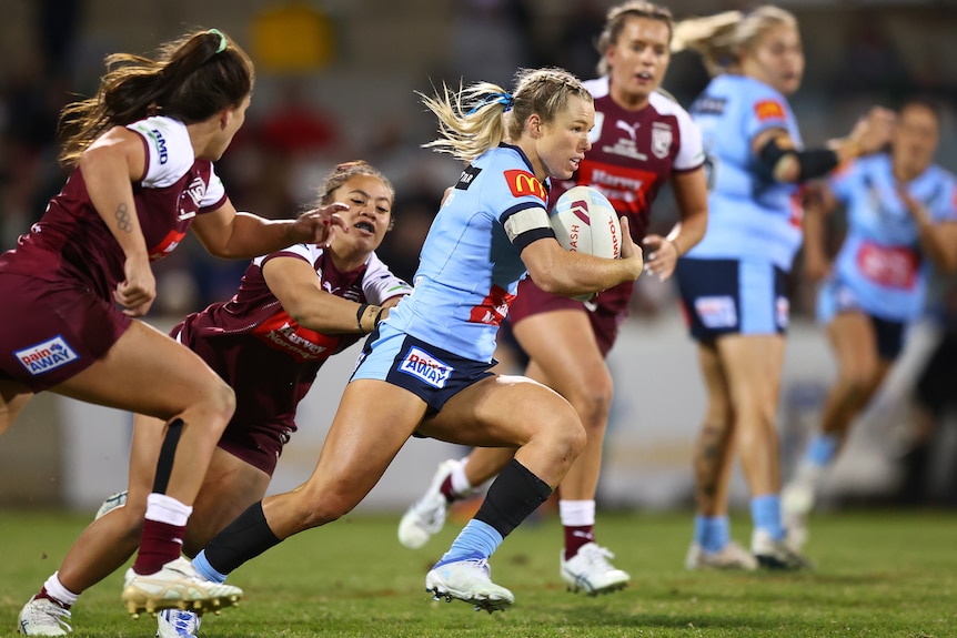 A NSW Women's rugby league player races up the field as Queensland players try to tackle her in State of Origin.