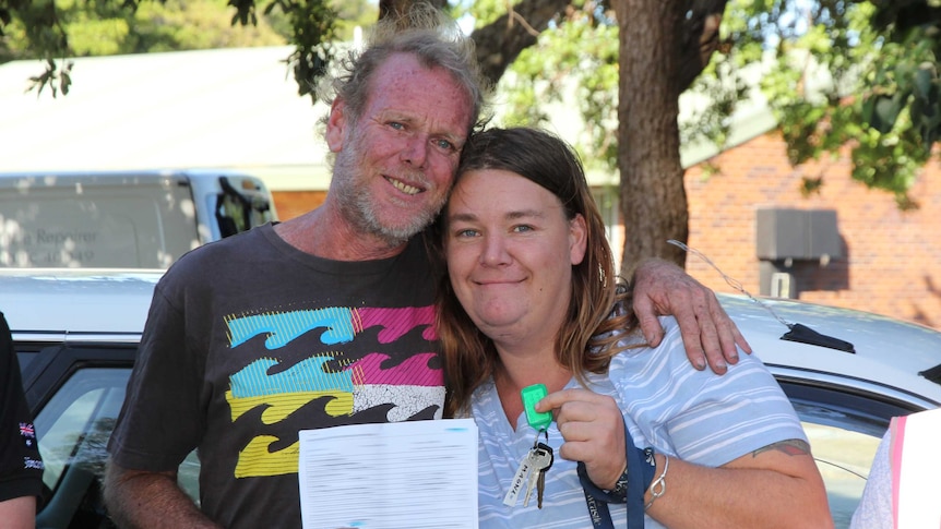 A homeless couple stand side by side with the keys to their new car