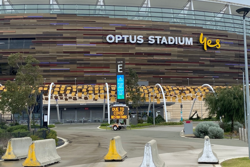 A photo of pedestrian blocks outside Perth stadium and a sign about COVID-19 in the background.