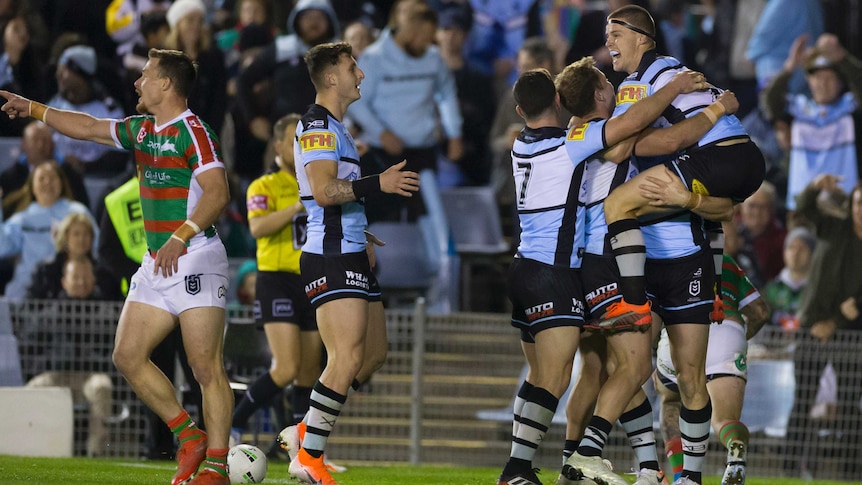 A grinning NRL player is lifted in the air by teammates after he scores a try.