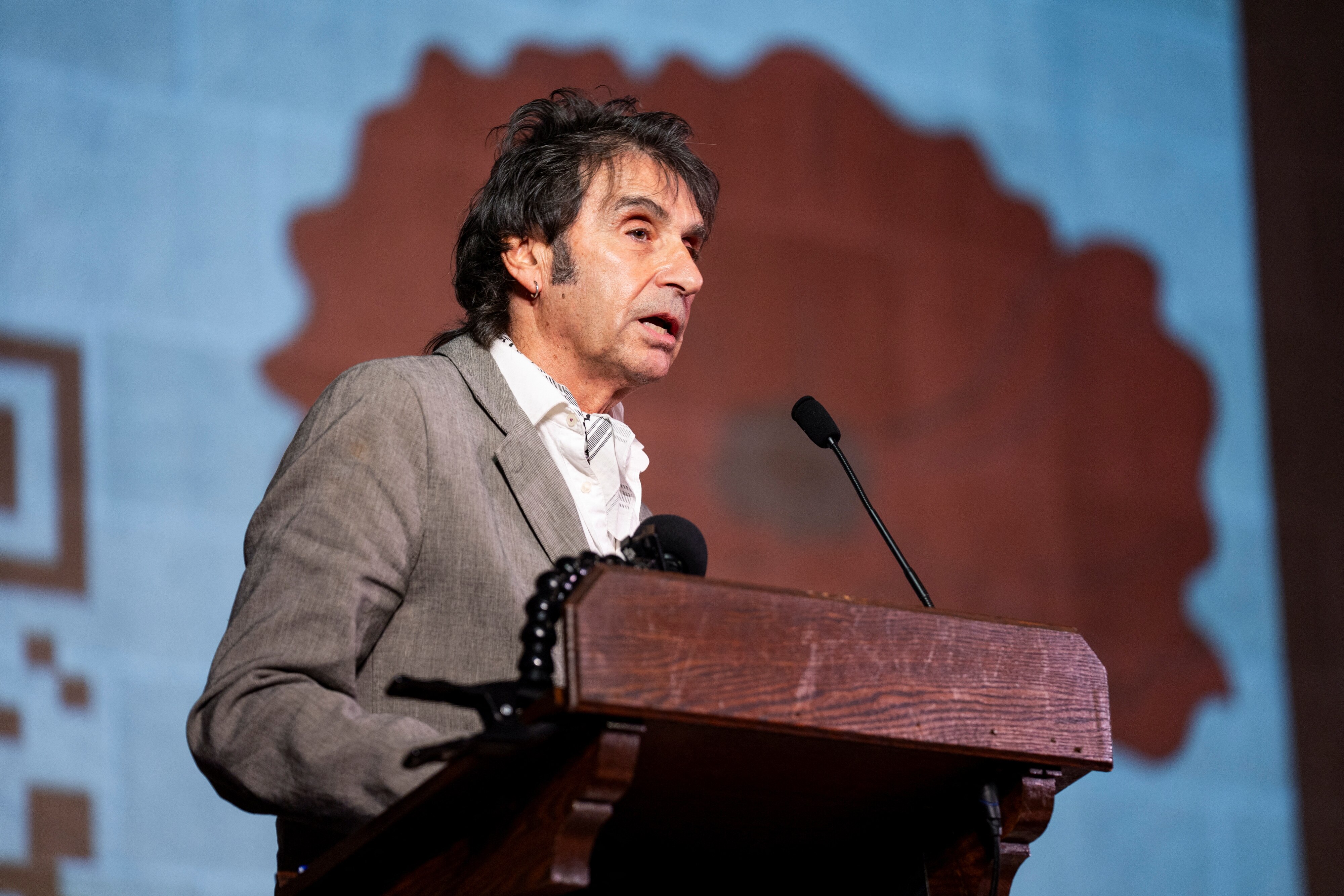 A man in a grey suit jacket speaks at a lectern