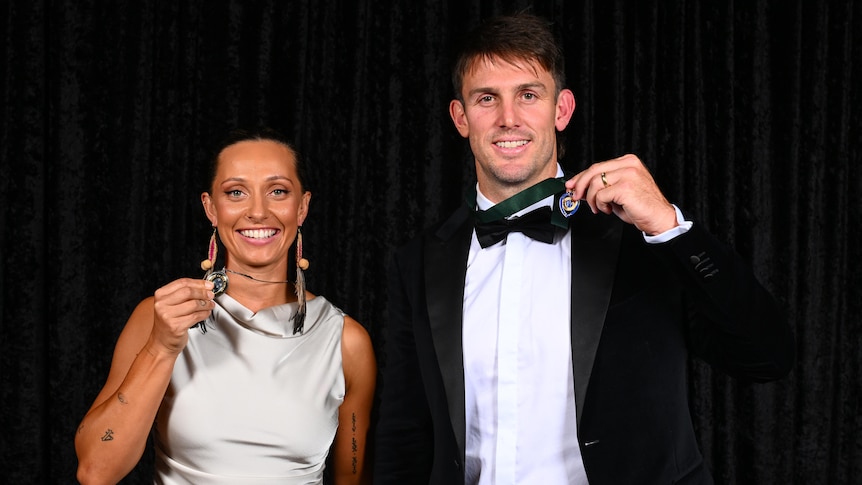 A woman and man pose smiling standing next to each other holding their respective cricket award medals.