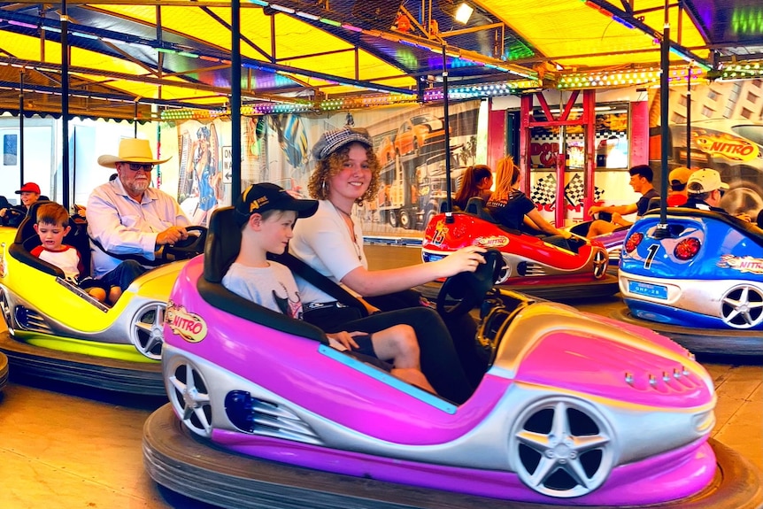 Two children, a boy and a girl, sitting in a car on a colourful show ride and smiling.