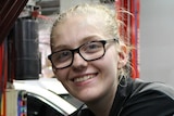 Charlotte Graham smiles has she holds tools while looking at a car engine