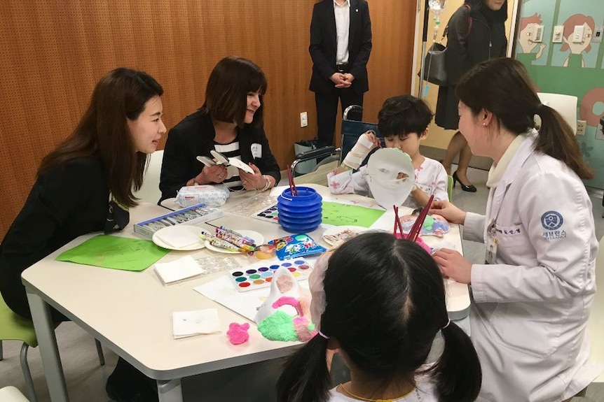 Karen Pence listens to a child who is painting a mask as part of an art therapy session in seoul