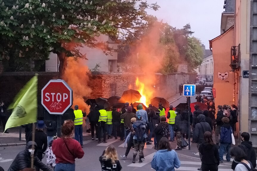 A fire burns as dozens of people, some wearing yellow vests, protest