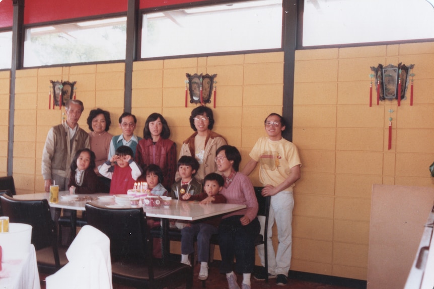 A film photo of a large family group smiling inside a Chinese restaurant.