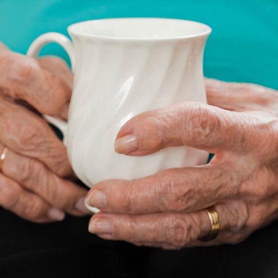A close-up of an older person's hands gripping a tea cup